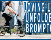 A woman riding a Brompton folding bike in her everyday clothes in a city setting