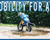A child coasting on a balance bike through a mud puddle